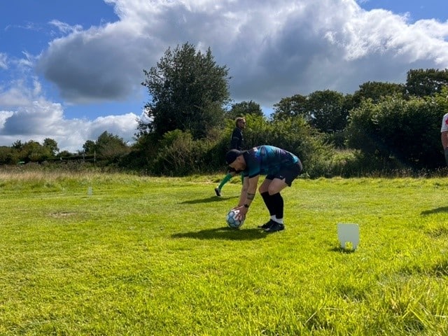 A man placing a football in position ready for him to kick into the footgolf course - health benefits