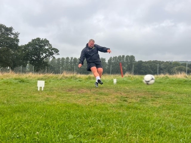 A man kicking a football from the start line of a footgolf course