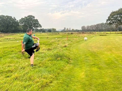 A man completing a kick of a football on a footgolf pitch to feel the health benefits