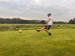 a boy kicking a yellow football on a footgolf pitch to improve his health benefits