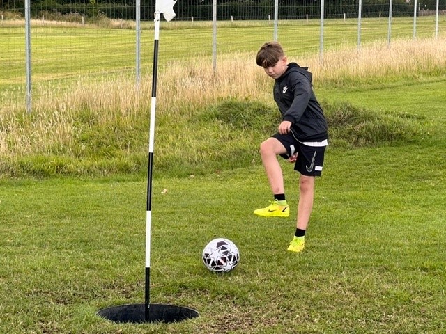 Guide to footgolf young boy kicking the football into the hole on the pitch
